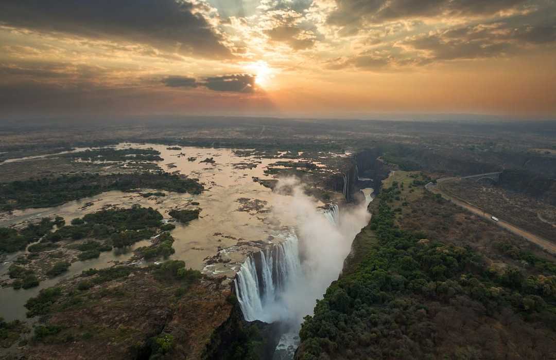 The mighty Victoria Falls cascades dramatically at sunset over Zambezi River.