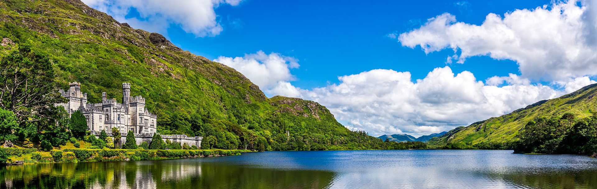 Beautiful castle like Kylemore Abbey reflected in lake at the foot of a mountain in Connemara, Ireland.