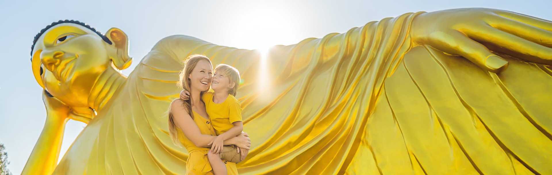 Mother and son on vacation pose in front of Lying Buddha statue in Thailand.