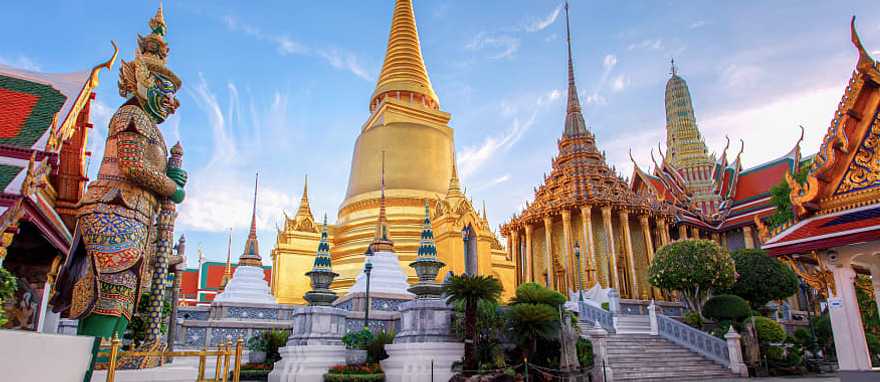 Grand Palace in Bangkok with golden stupa and ornate temples in Wat Phra Kaew at sunset.