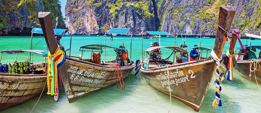 Wooden boats in the turquoise waters of Maya Bay with limestone karst cliffs on Phi Phi island in Thailand