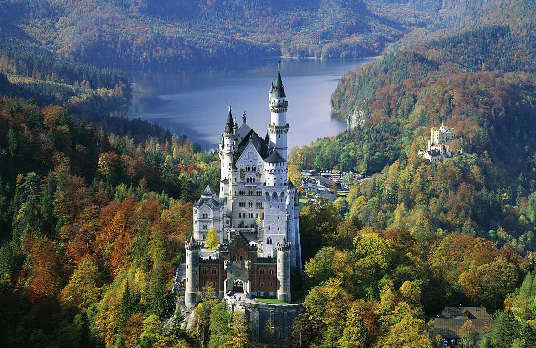 Neuschwanstein Castle in Bavaria, Germany, surrounded by autumn forest and overlooking a mountain lake