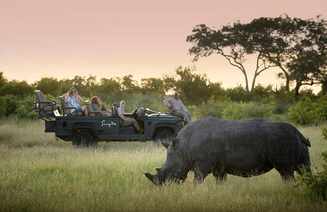 Private game drive at Castleton Luxury Lodge & Safari in Sabi Sands, South Africa. Photo courtesy of Singita "Travelers on a safari game drive watch a rhinoceros grazing in the South African bushveld