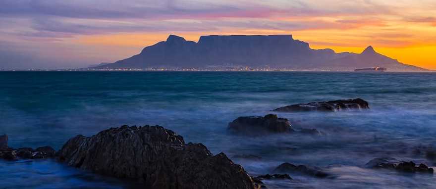 Silhouette of Table Mountain against sunset sky and ocean waves in Cape Town, South Africa Silhouette of Table Mountain against sunset sky and ocean waves in Cape Town, South Africa