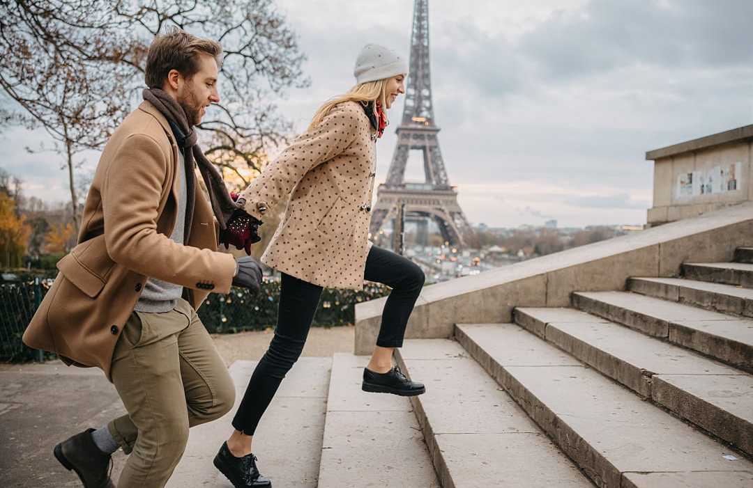 Romantic couple standing in front of the Eiffel Tower in Paris, France, under a cloudy sky, with the iconic monument towering in the background