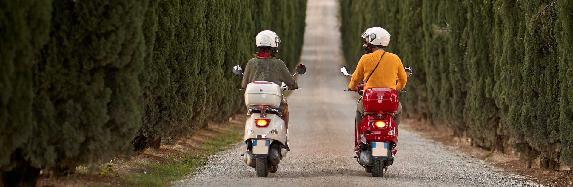 A couple on scooters on a tree-lined street in Tuscany