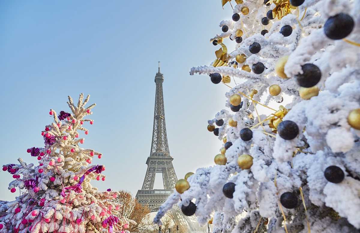 Snow-covered Christmas trees decorated with ornaments with the Eiffel Tower in the background, capturing the festive holiday in Paris, France