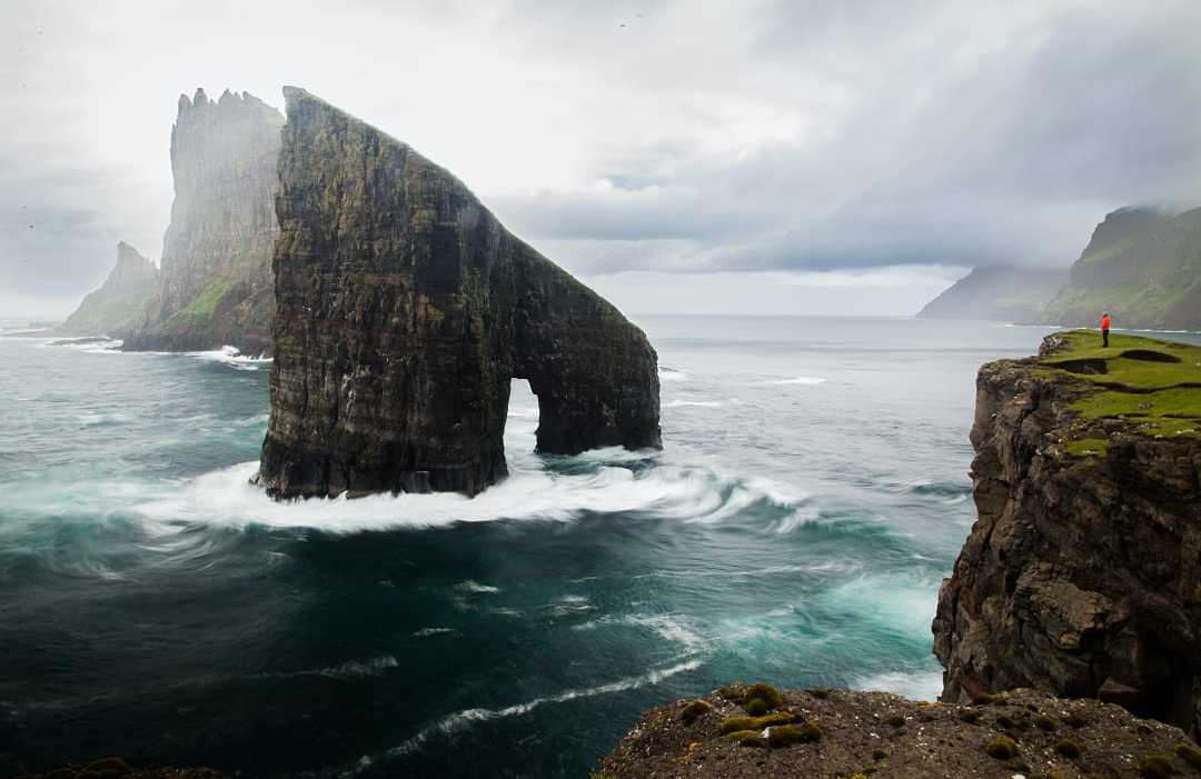 Drangarnir sea stacks rising from the Atlantic Ocean near Vágar, Faroe Islands, with dramatic cliffs and waves crashing below.