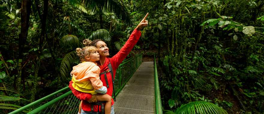 "Mother and child on a rainforest walkway in Arenal, Costa Rica, exploring and pointing at the lush greenery.