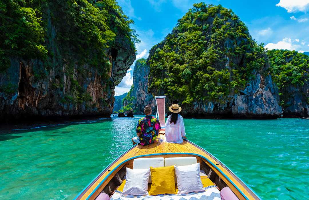 Couple on a traditional boat exploring turquoise waters and limestone cliffs in Krabi, Thailand