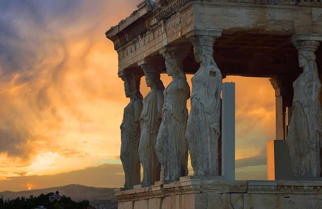 Caryatid statues support Erechtheion porch at sunset in Athens.