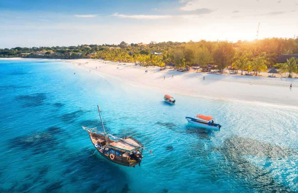 Boats on tropical sea coast with sandy beach at sunset in Tanzania, Zanzibar on the continent of Africa