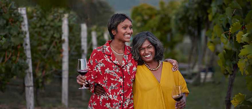 Smiling mother and daughter holding wineglasses and standing with arms around each other at a vineyard Smiling mother and daughter holding wineglasses and standing with arms around each other at a vineyard
