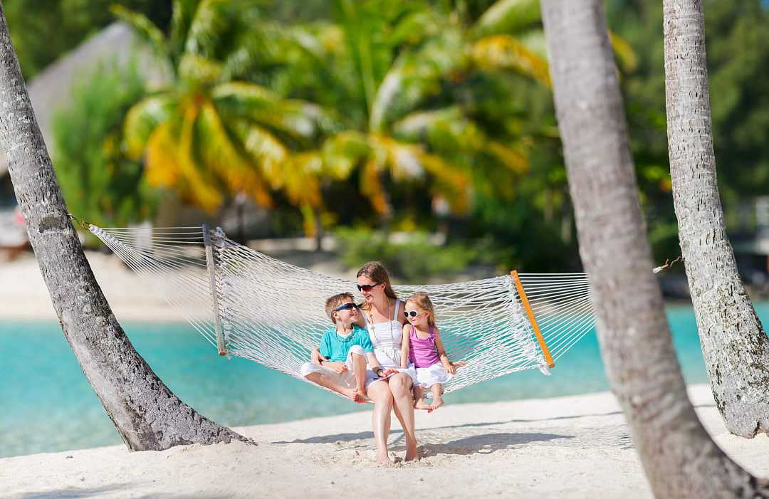 French Polynesia Mother swinging in a hammock on the beach with her kids in French Polynesia
