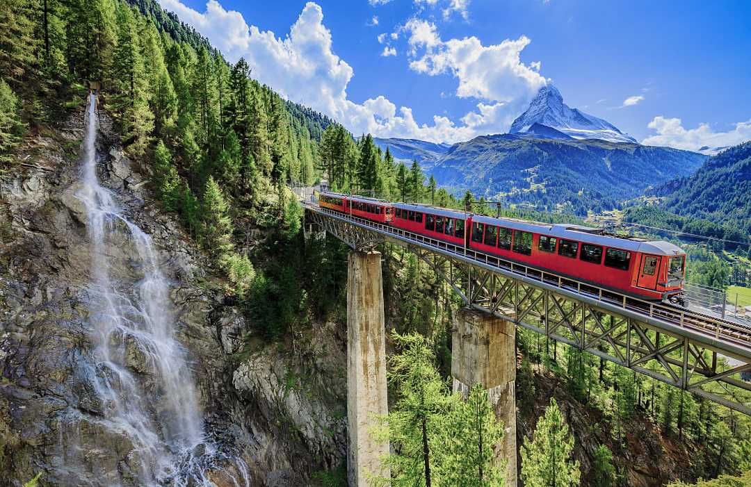 A red train crossing a high mountain bridge in Switzerland.