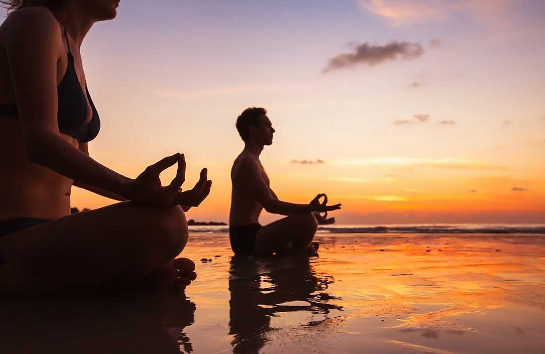 A couple practicing some meditation during a sunrise in French Polynesia.