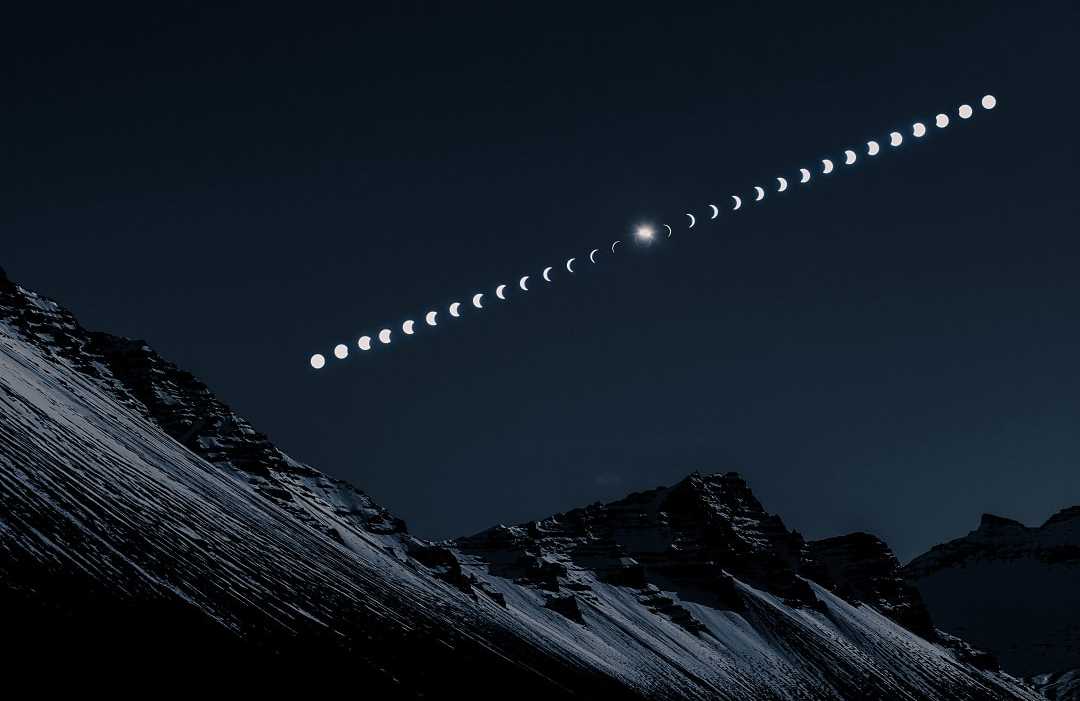 Composite image showing the phases of a solar eclipse over snow-covered mountain peaks at night.