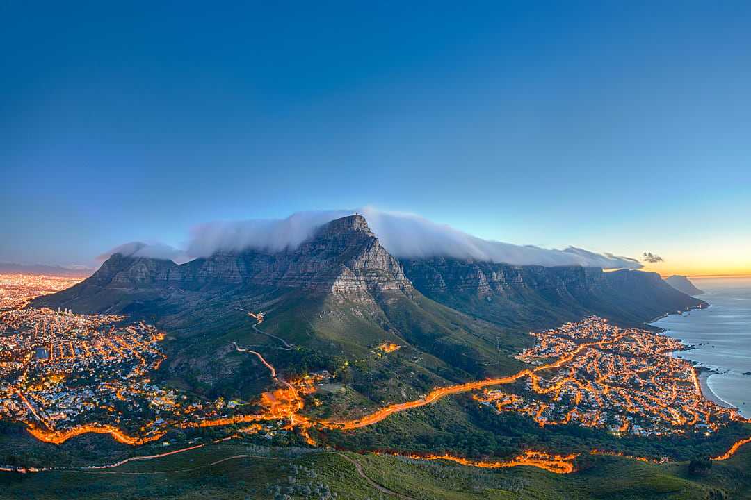 Stunning aerial view of Table Mountain, Cape Town, at sunset with city lights and clouds over the peak