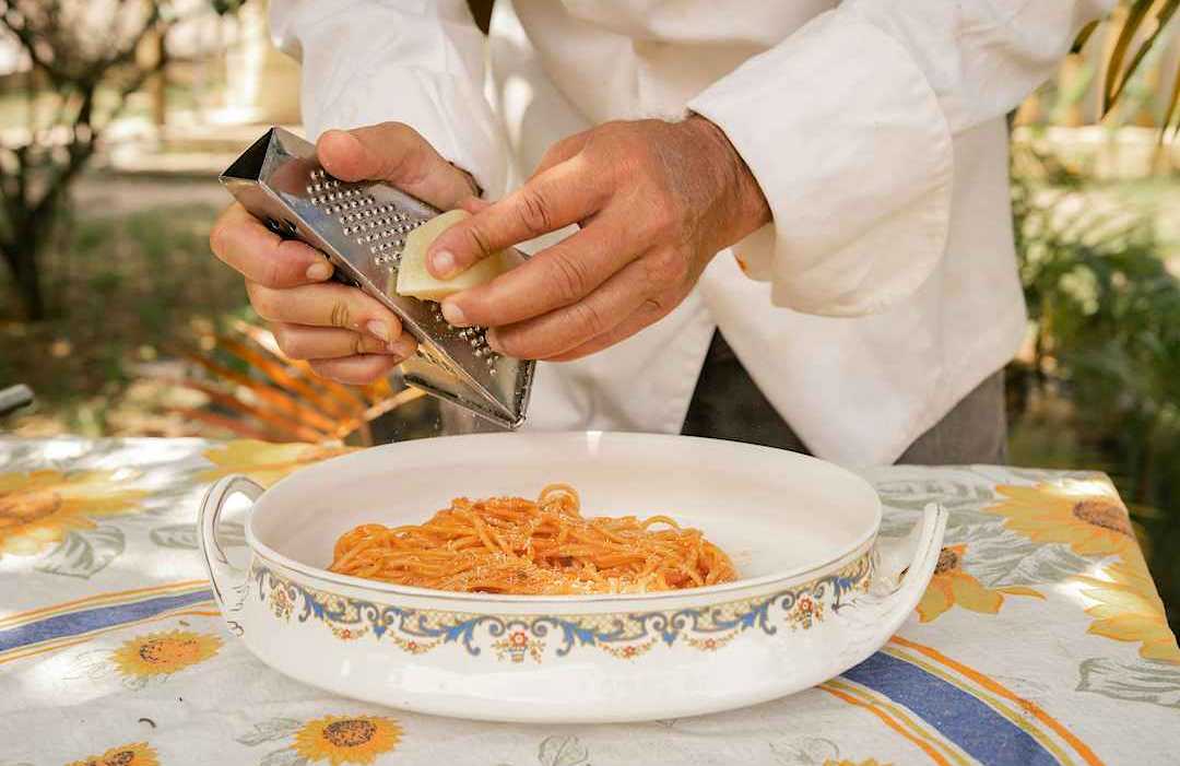 Chef grating Parmigiano cheese over a plate of pasta, Italy.