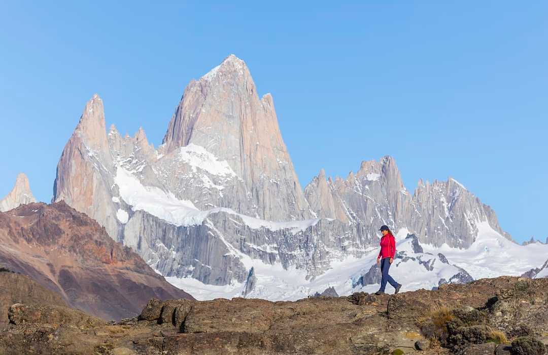 Hiker in red jacket walking with Mount Fitz Roy in Patagonia's stunning landscape as the backdrop