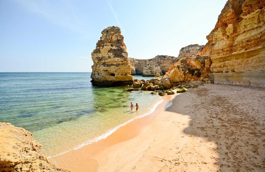 Couple in the water surrounded by limestone cliffs at Praia da Marinha in the Algarve